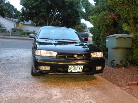 1998 Subaru Legacy - A black 1998 Subaru Legacy is parked in a driveway, showing its front grille and headlights.