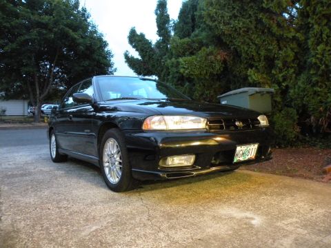1998 Subaru Legacy - A black 1998 Subaru Legacy is parked on a driveway, showing its front grille and license plate.