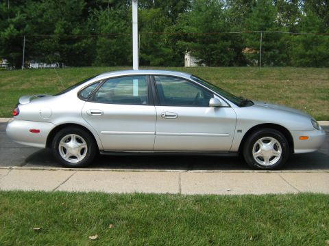 1988 Mercury Grand Marquis - This silver sedan is shown from the side, parked next to a grassy area and curb.