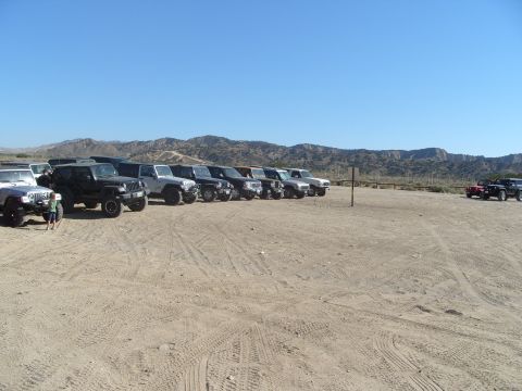 1995 Ford Bronco - Several off-road vehicles are parked in a dusty lot under a clear blue sky.