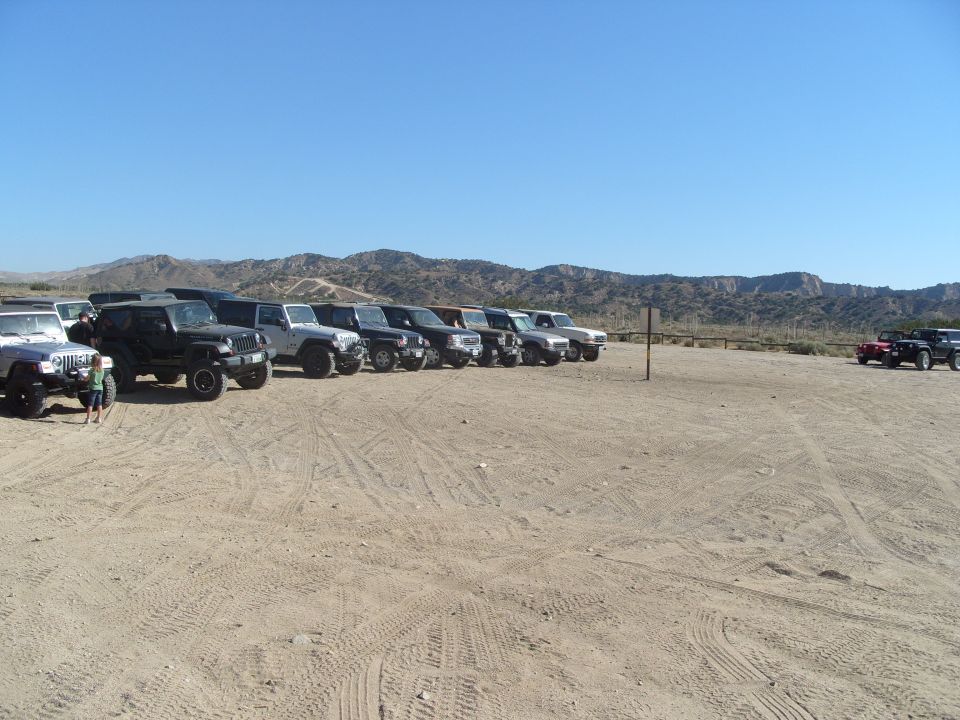 Multiple SUVs and trucks parked in a dirt lot with hills in the background