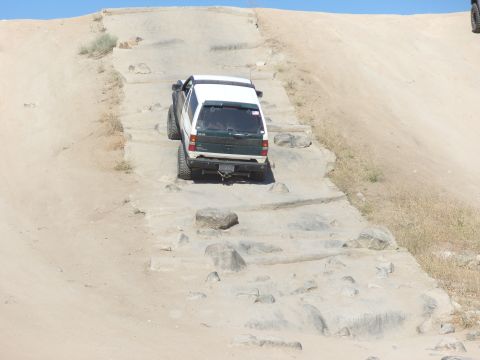 1995 Ford Bronco - A white and green SUV navigates a challenging rocky terrain on a sunny day.