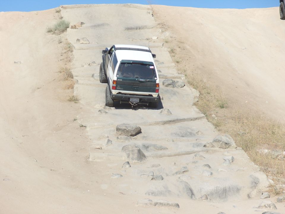 White and green SUV with aftermarket wheels driving on a rocky, sandy incline