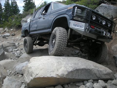 1991 Ford Bronco - Pickup truck with custom bumper and lights is shown off-roading over large boulders.