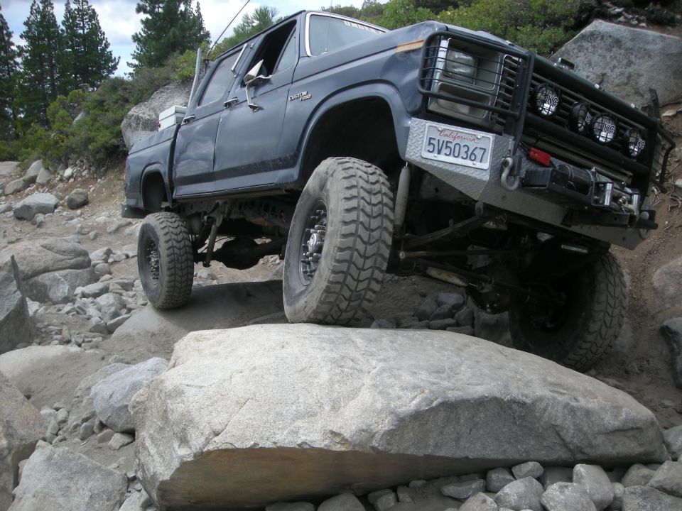 Modified pickup truck with large tires navigating large rocks off-road. License plate reads 5V50367