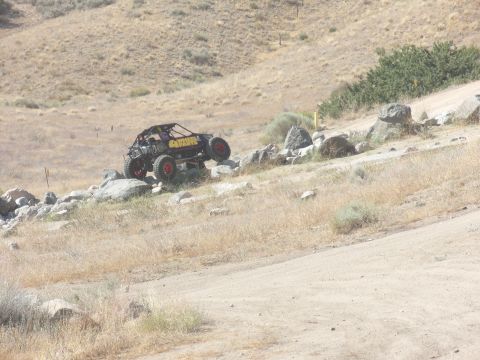 1995 Ford Bronco - A custom off-road buggy navigates a rocky trail in a dry, hilly landscape.