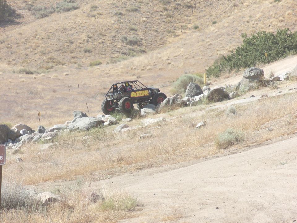 Custom off-road buggy with roll cage and large tires climbing a rocky incline