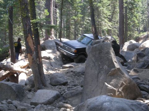 1991 Ford Bronco - A black 1991 Ford Bronco is shown navigating a challenging rocky trail in a wooded area.