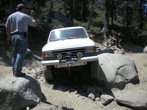 1991 Ford Bronco - A white Ford truck navigates a challenging rocky trail with a person observing.