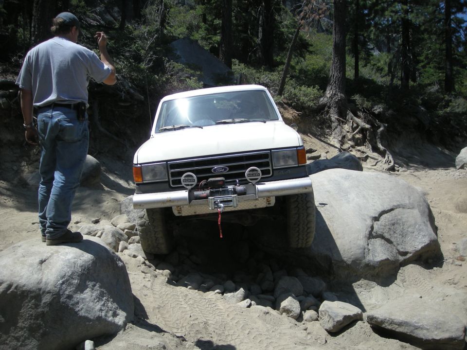 White Ford truck with winch on rocky terrain, front view