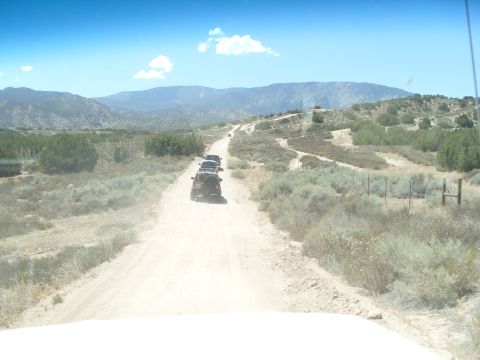 1995 Ford Bronco - A convoy of SUVs travels down a dusty road through a dry, mountainous landscape under a bright blue sky.