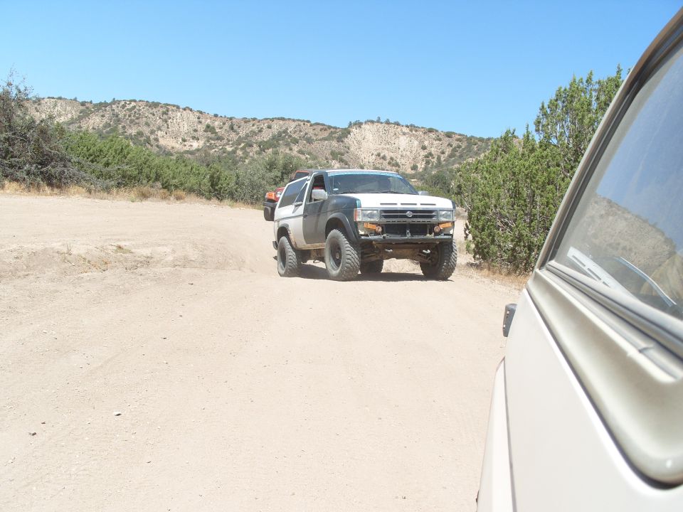 Off-road Nissan Pathfinder driving on dirt road with another vehicle in foreground