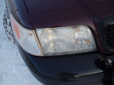 1999 Ford Crown Victoria - Close-up of the front corner of a dark red vehicle, showing the headlight and turn signal assembly.