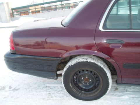 1999 Ford Crown Victoria - Rear quarter panel view of a maroon sedan with a black bumper and a wheel covered in snow. The body style suggests a 1998 Ford Crown Victor…