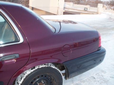 1999 Ford Crown Victoria - Rear view of a maroon sedan with a black bumper and gas cap, seen in a snowy environment.