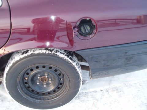 1999 Ford Crown Victoria - The rear quarter panel and wheel well of a dark red vehicle are visible, with the fuel door open, in a snowy environment.