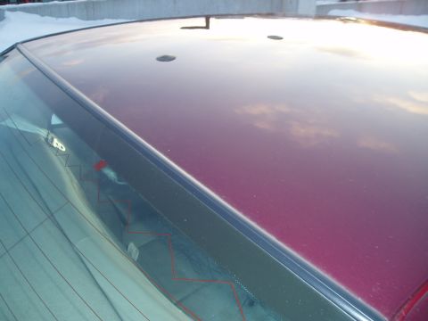 1999 Ford Crown Victoria - The reflection on the car's roof shows a cloudy sky. The rear window has defroster lines.