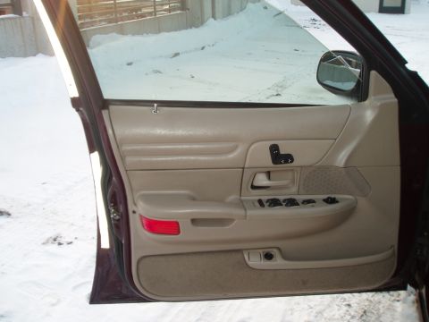 1999 Ford Crown Victoria - The interior door panel of a vehicle, beige trim and power window controls, is shown in a snowy environment.