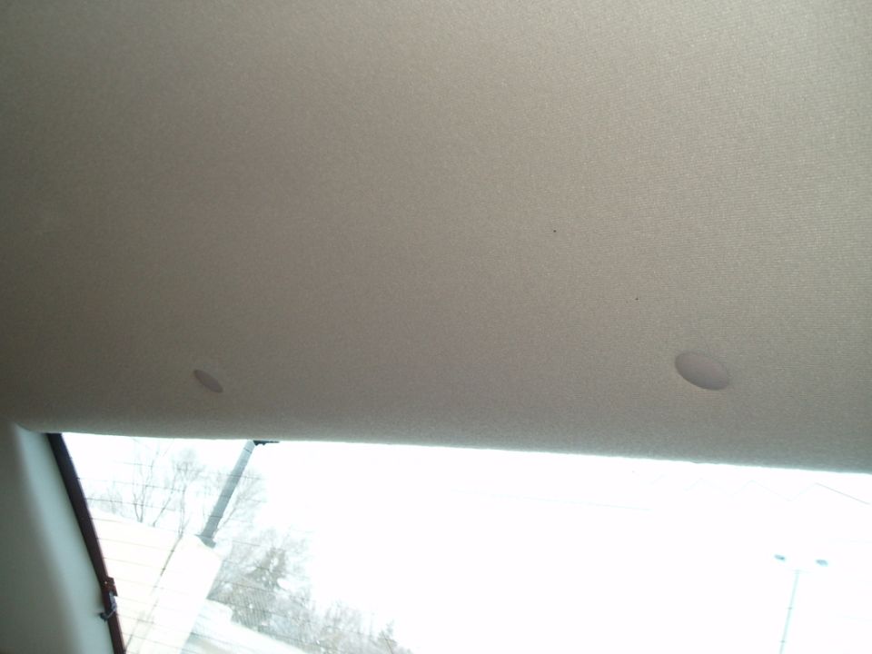 Car interior ceiling with two small speaker grilles and a water stain, viewed from below