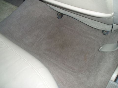 1999 Ford Crown Victoria - The interior floor of a car shows gray carpeting with some dirt and stains.