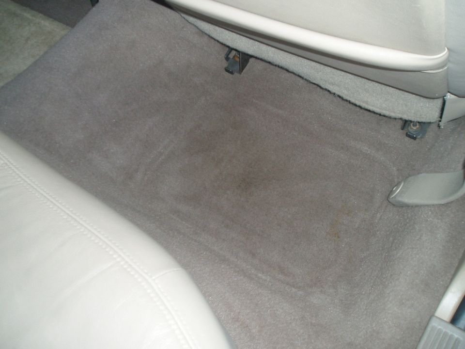 Car's gray carpeted floor with some stains. White leather seat is visible on the left
