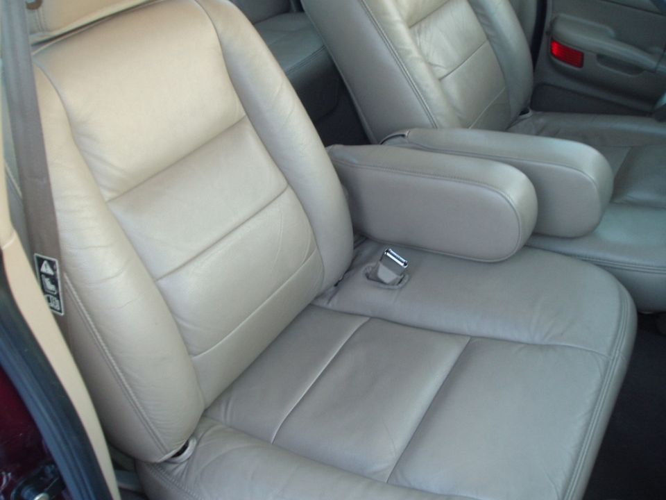 Car interior with tan leather seats and armrests. A red taillight is visible in the background