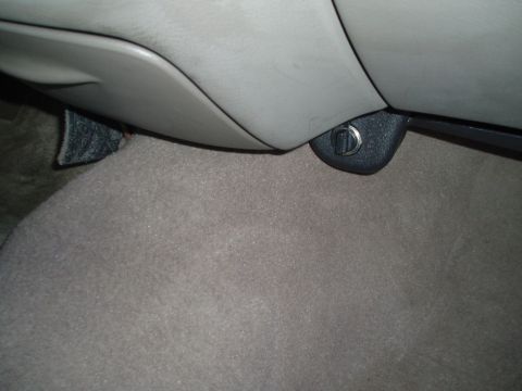 1999 Ford Crown Victoria - Close-up of a car's interior, focusing on a latch mechanism near the floor.