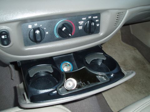 1999 Ford Crown Victoria - Close-up of a car's center console, climate control knobs and a compartment with cup holders and a power outlet.