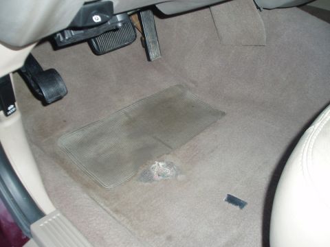1999 Ford Crown Victoria - The driver's side floor area shows pedals, a floor mat, and worn carpeting.