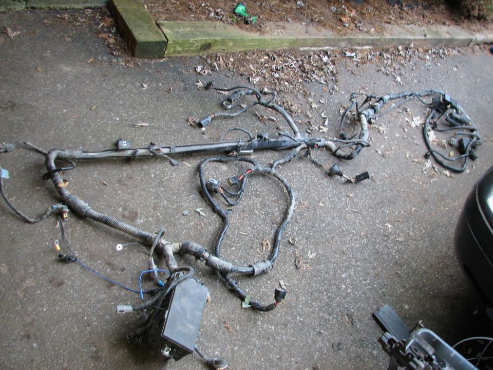 Engine wiring harness laid out on asphalt, with a black fuse box attached
