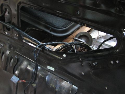 1999 Ford Crown Victoria - Close-up inside a stripped car body at the rear parcel shelf/package tray area, with the trim removed to expose bare black sheet metal, an…