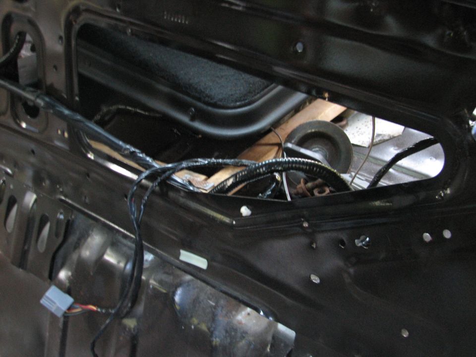 Bare metal rear package tray of stripped car with exposed wiring loom and speaker magnet