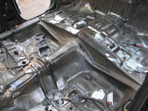 1999 Ford Crown Victoria - Stripped interior floor pan of a car, revealing the metal structure and wiring harnesses.