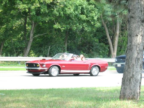 1988 Mercury Grand Marquis - A red 1969 Ford Mustang convertible cruises down the road with passengers enjoying the ride.