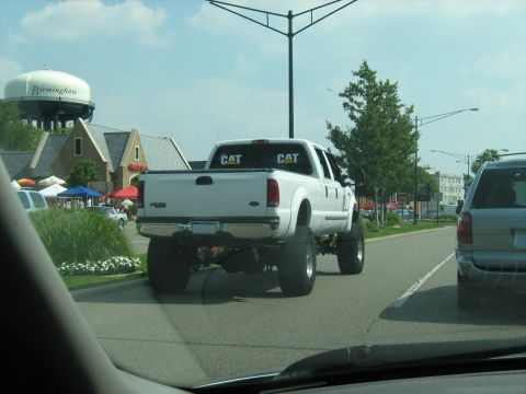 1988 Mercury Grand Marquis - A lifted white pickup truck with "CAT" decals is seen from the rear on a sunny day.