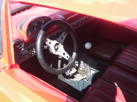1988 Ford Bronco - The interior of a custom vehicle features a steering wheel, shifter, and red upholstered seats.