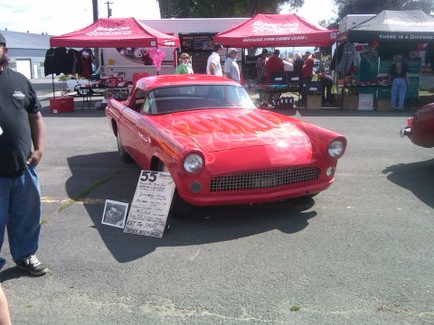 1988 Ford Bronco - A red 1955 Ford Thunderbird with flame graphics is displayed at an outdoor car show.