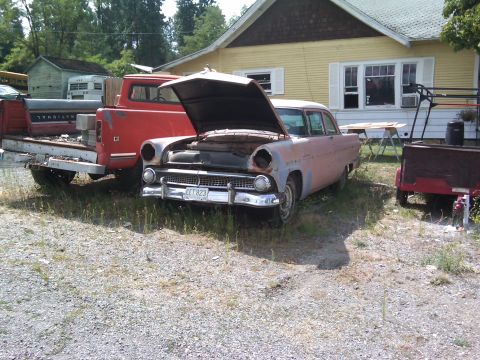1988 Ford Bronco - A weathered 1955 sedan sits in a yard with its hood up, beside a red pickup truck.