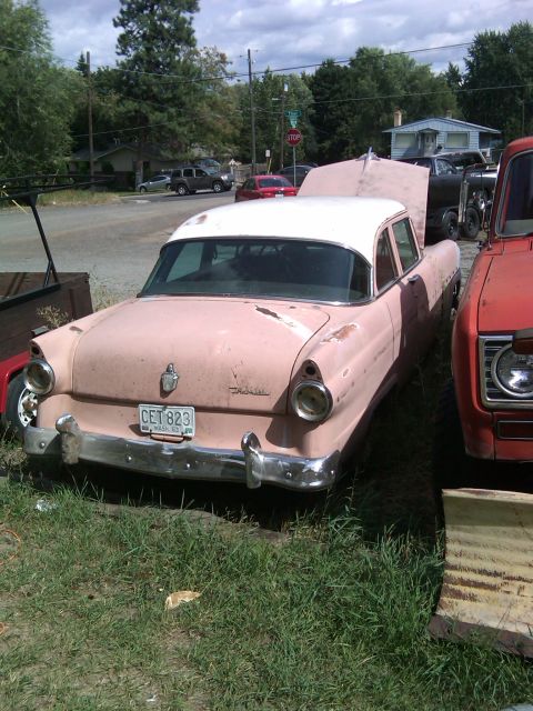 1988 Ford Bronco - A pink sedan with its hood open is parked next to a red truck in an outdoor lot.