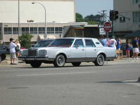 1988 Mercury Grand Marquis - A classic Lincoln Town Car is seen from the side on a sunny day with people nearby.