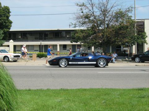 1988 Mercury Grand Marquis - A blue sports car drives down the street past a motel, with other vehicles and pedestrians present.