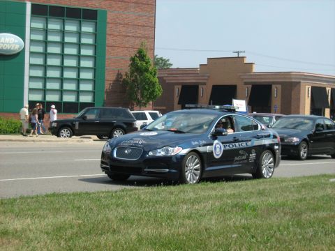 1988 Mercury Grand Marquis - A Jaguar police car is seen on the road, with a Range Rover parked on the side near a building.