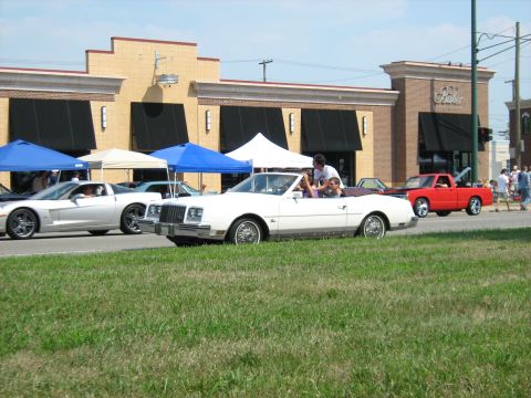 1988 Mercury Grand Marquis - A white convertible cruises down the street with other vehicles and people in the background.