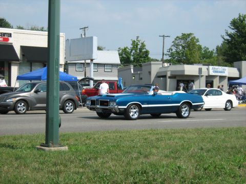 1988 Mercury Grand Marquis - A blue convertible cruises down the street alongside other vehicles on a sunny day.
