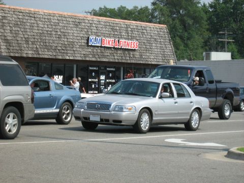 1988 Mercury Grand Marquis - A silver sedan is seen from the front, parked in front of a KLM Bike & Fitness store.