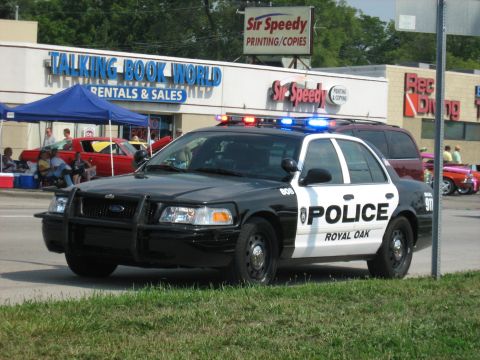 1988 Mercury Grand Marquis - A Royal Oak police car is parked outside a strip mall with 'Talking Book World' visible.