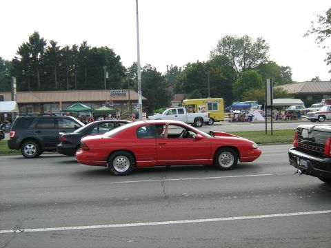 1988 Mercury Grand Marquis - A red coupe with a modified hood is seen driving alongside other vehicles during an event.