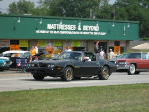 1988 Mercury Grand Marquis - A black 1977 Pontiac Firebird Trans Am is seen driving in front of a Mattress & Beyond store.