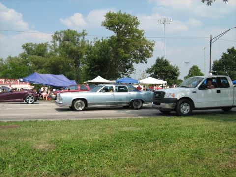 1988 Mercury Grand Marquis - A light blue sedan and a white pickup truck are seen on the road during an outdoor event.