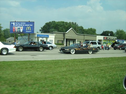 1988 Mercury Grand Marquis - A customized black convertible with flame decals cruises down the road alongside other vehicles.